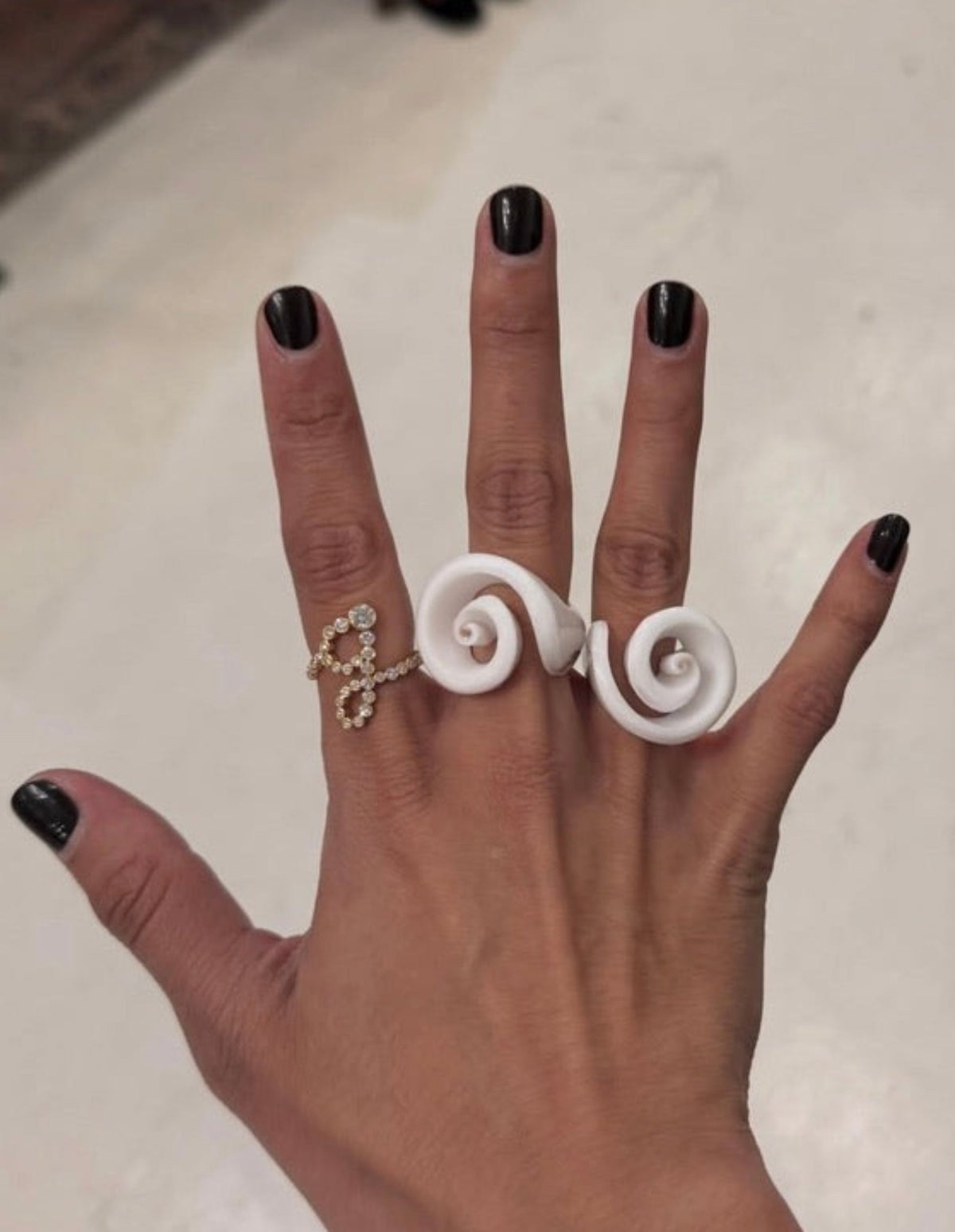 Closeup of a hand wearing a white double spiral shell ring and a delicate crystal accent ring by Kat Zarra from New Arrivals