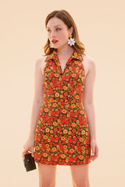 Woman wearing a Miracle Eye floral mini dress with a collared neckline and sleeveless cut while carrying a black handbag against a warm peach background