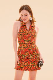 Woman wearing a vibrant floral halter mini dress in marigold with a metallic clutch in a warm studio setting from Miracle Eye