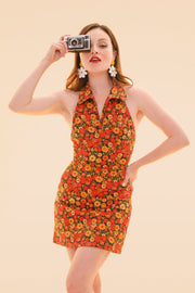 Woman in a marigold floral halter mini dress holds a vintage camera in a bright studio image from Miracle Eye New Arrivals and Sustainable Dresses and One Pieces