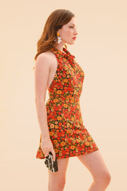 Woman wearing a vibrant floral halter mini dress and holding a small clutch for a sunny summer look from Miracle Eye