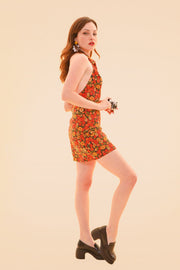 Model wearing a floral marigold mini dress with a halter neckline and brown platform sandals in a warm studio setting from Miracle Eye