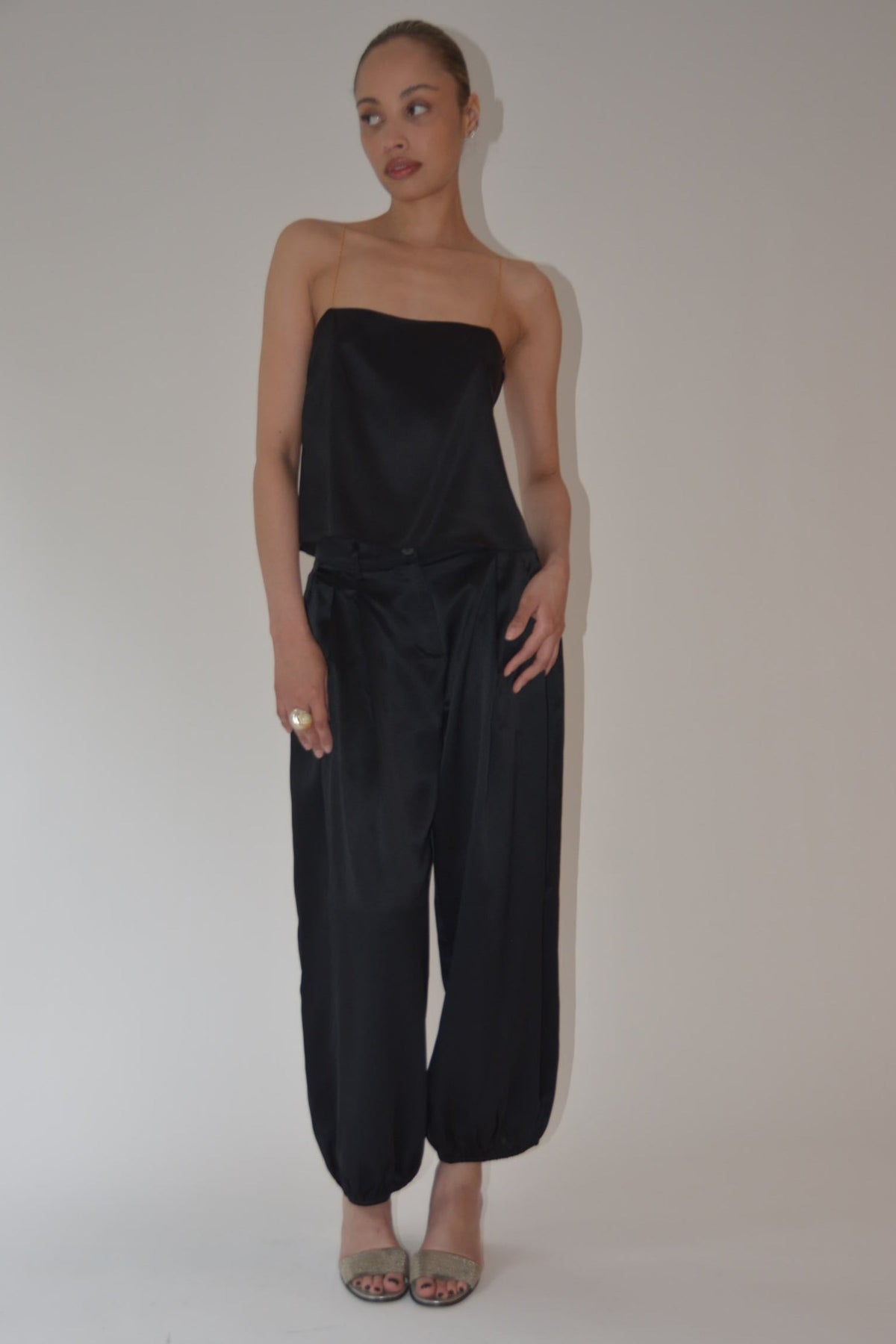 Model wearing black silk balloon pants with relaxed draping and tapered ankles styled with a strapless black top and open toe sandals by Kat Zarra