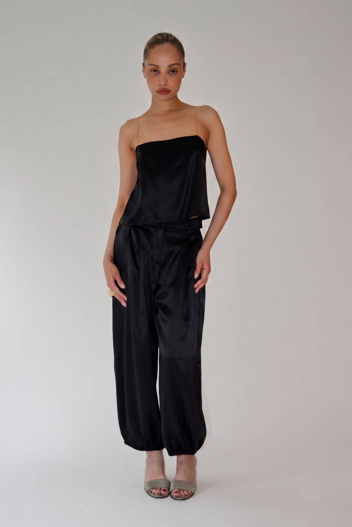 Model wearing black silk balloon pants with fluid draping and tapered ankles styled with a strapless top and sandals from Kat Zarra