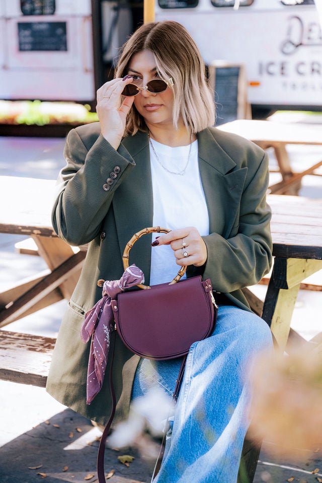 Margo Paige burgundy vegan cactus leather semi circle crossbody bag worn with a casual outfit in a cafe setting from New Arrivals