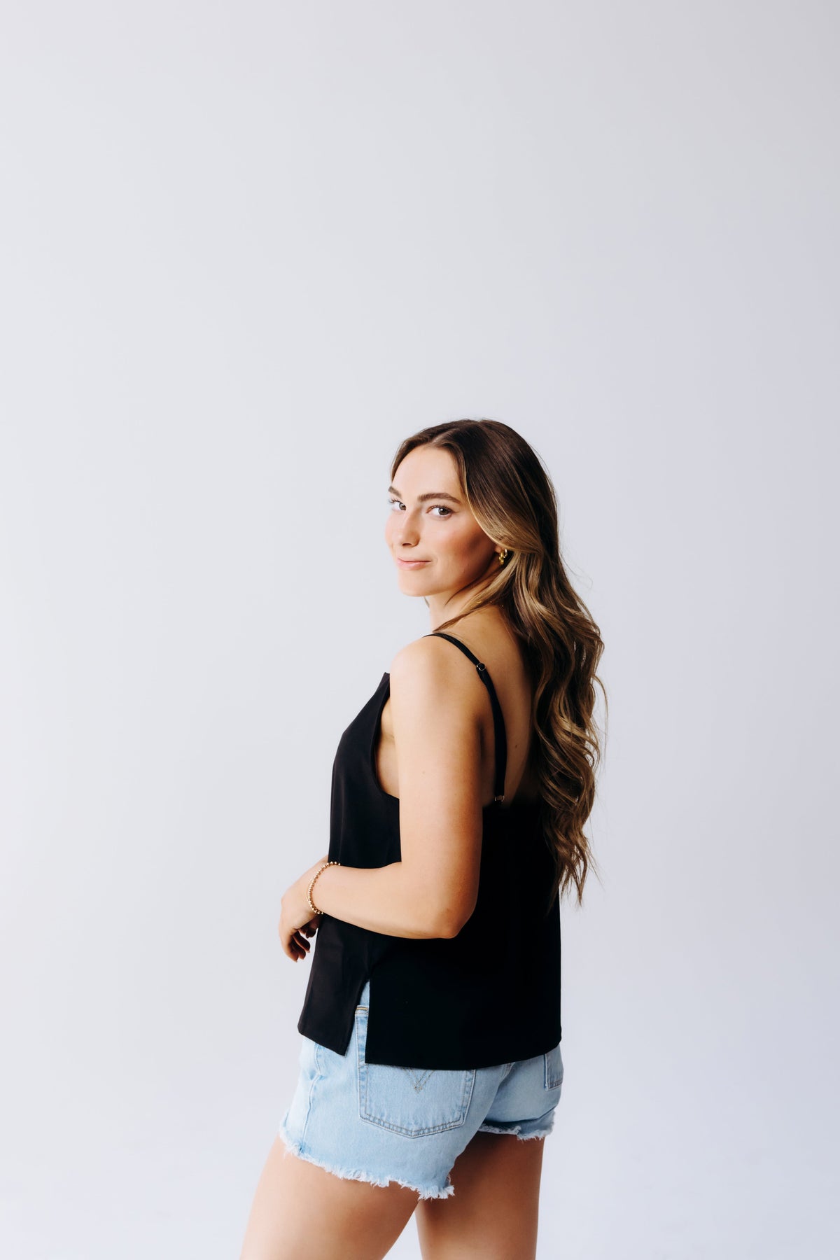 Margo Paige black cowl neck cami with adjustable straps styled with light denim cutoff shorts on a model against a neutral background
