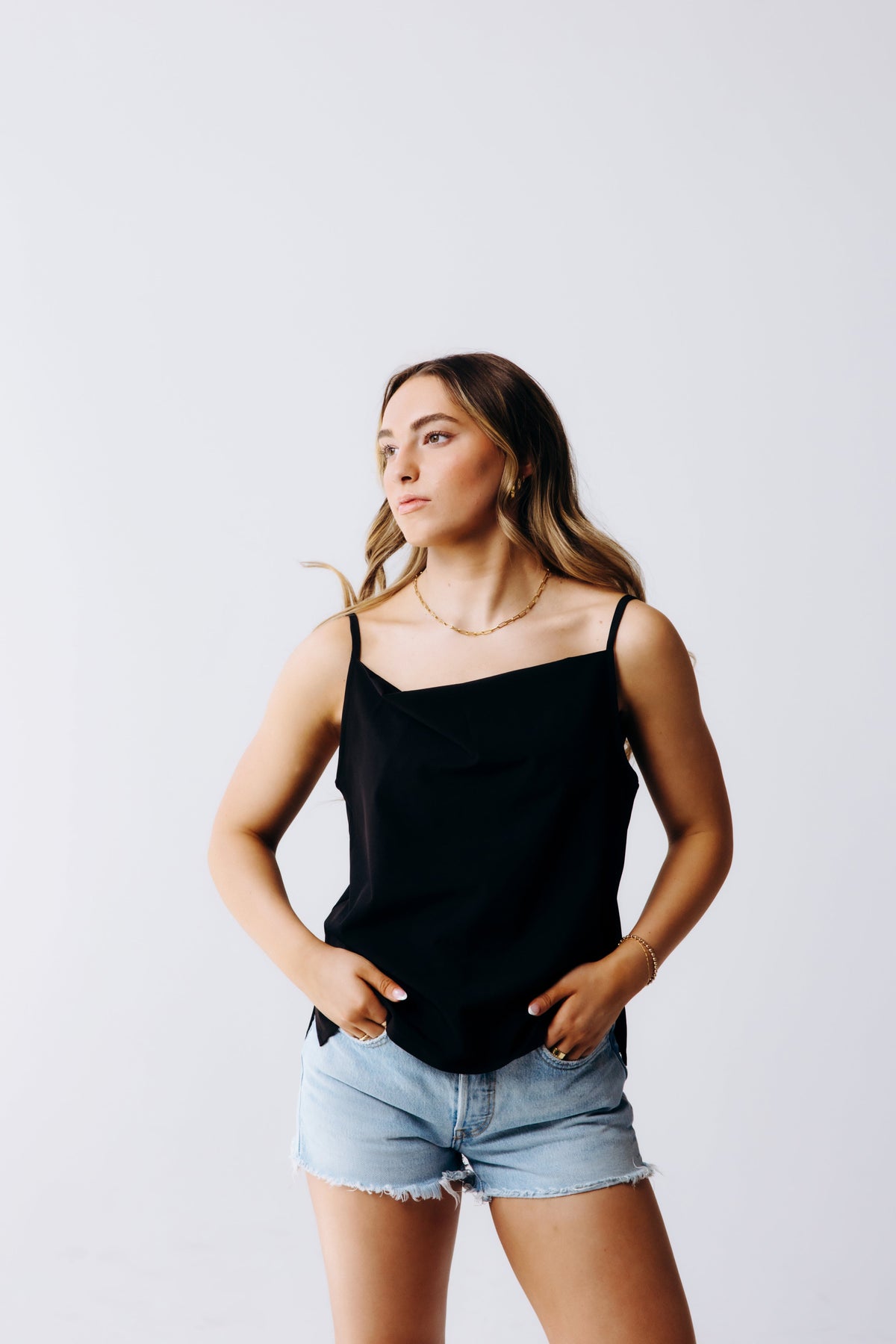 Margo Paige model wearing a black cowl neck cami with adjustable straps styled with light wash denim shorts against a clean studio backdrop