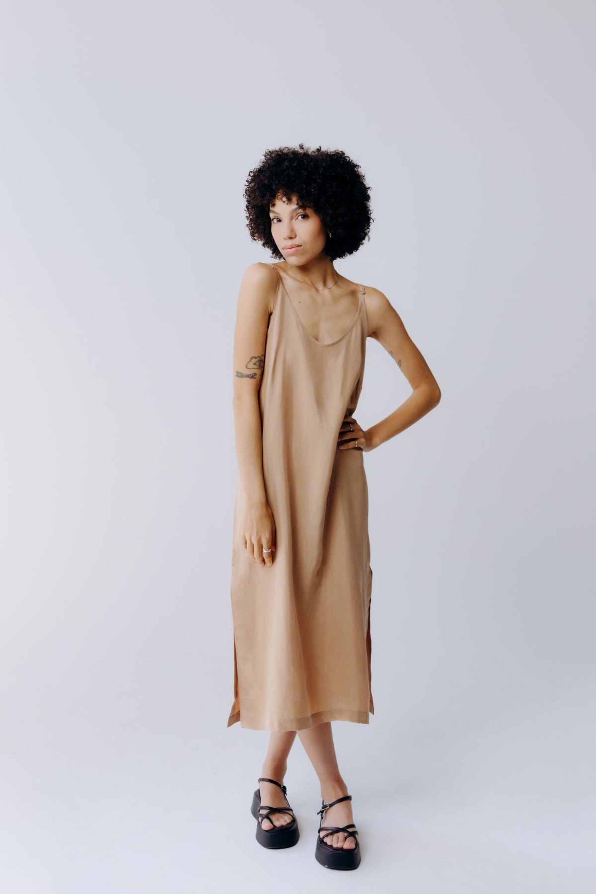 Model wearing a tan washable silk midi dress with a relaxed silhouette and black strappy sandals from Margo Paige sustainable new arrivals