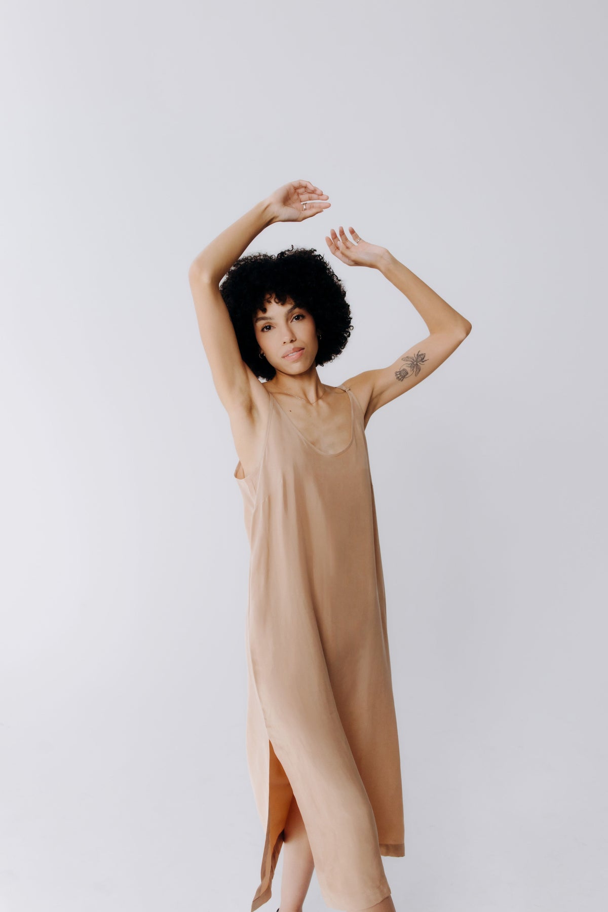 Margo Paige model wearing a tan sleeveless midi dress with a side slit against a light gray studio background